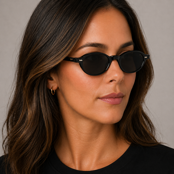 Ellipse Eco Black Grey oval sunglasses with dark lenses worn by female model in her 30s, close-up studio portrait styled with a black T-shirt, highlighting the slim eco-acetate frame and refined silhouette.