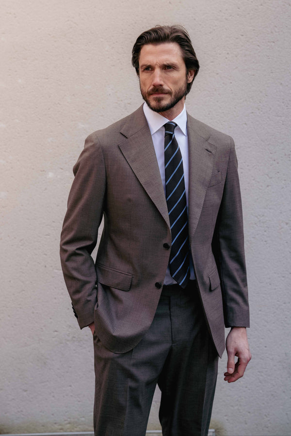 Man wearing a brown suit and striped tie against a plain background | Andréa Kọsta